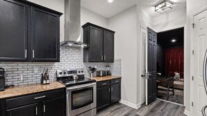A modern kitchen with dark cabinetry, a stainless steel stove, and a brick backsplash. - Reflections Manor at Reunion | Stay in style at 5-bedroom villa in Orlando Near Disney (Kissimmee)