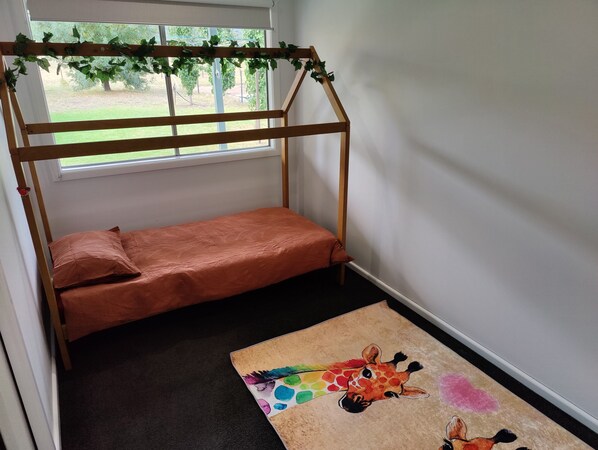 A child's bunk bed with a wooden frame and orange bedding, a colorful giraffe rug, and a view of a green outdoor area through a window.