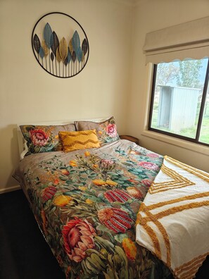 A bedroom with a floral bedspread, a decorative wall piece, and a window with a view of the outdoors. - Charming country cottage, peaceful stay, family-friendly retreat, Glenrowan (Glenrowan)