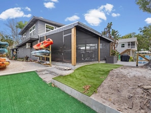Ett modernt hus med en inglasad veranda, en välskött gräsmatta och en kajak på verandan.