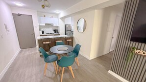 Een moderne keuken met witte kasten, een eethoek met een ronde tafel en teal-kleurige stoelen, en een televisie aan een gestreepte muur.