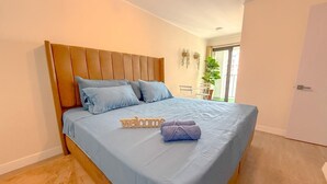 Een bed met hoofdbord, kussens, een welkomstbord en een opgerolde handdoek.