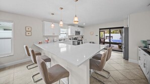 A modern kitchen with a large island, pendant lights, and a view to the outside. - Naples Paradise - Heated Saltwater Pool/Spa, Walk/Bike to the Beach! (Naples)