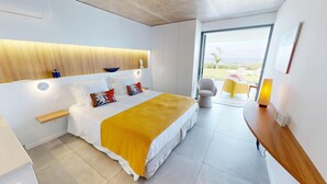Ein modernes Hotelzimmer mit Bett, Nachttisch, Lampe und Blick aufs Meer.