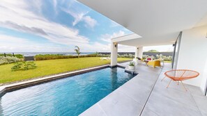 A modern outdoor pool area with a view of the ocean, a grassy lawn, and outdoor furniture. - Vaguelis - Beachfront Villa in Le Moule (Aquawaves) (Le Moule)
