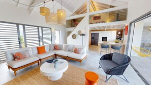 A modern living room with a sectional sofa, a round coffee table, and a dining area with bar stools. - Vaguelis - Beachfront Villa in Le Moule (Aquawaves) (Le Moule)