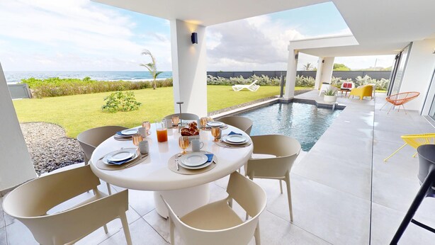 Ein moderner Essbereich im Freien mit Pool, Meerblick und einer Terrasse mit Stühlen und Tisch, gedeckt für eine Mahlzeit.