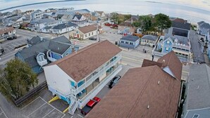 An aerial view of a coastal town with a prominent building featuring a two-story structure with a flat roof, a parking lot, and a visible road. - 70 E Grand OOB | 2BR Condo Steps to the Beach (Old Orchard Beach)