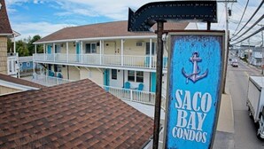 A multi-story building with a sign for 'Saco Bay Condos' featuring an anchor symbol. - 70 E Grand OOB | 2BR Condo Steps to the Beach (Old Orchard Beach)