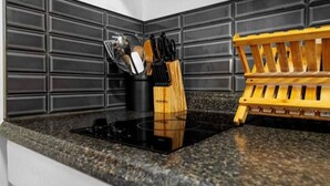 A kitchen with a black stovetop, granite countertop, black backsplash, and wooden utensil holder. - 70 E Grand OOB | 2BR Condo Steps to the Beach (Old Orchard Beach)