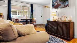 A living room with a sofa, a dining table with chairs, a TV mounted on the wall, and a cabinet. - 70 E Grand OOB | 2BR Condo Steps to the Beach (Old Orchard Beach)
