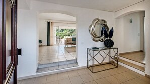 Een ruime hal met een trap, een moderne console tafel en een uitzicht op een woonkamer met een bank en een eettafel.