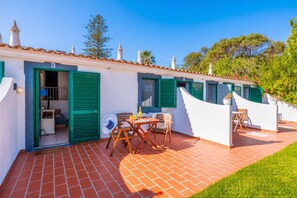 Un edificio blanco con contraventanas verdes, un patio con mesa y sillas, y el número 6 en la puerta.