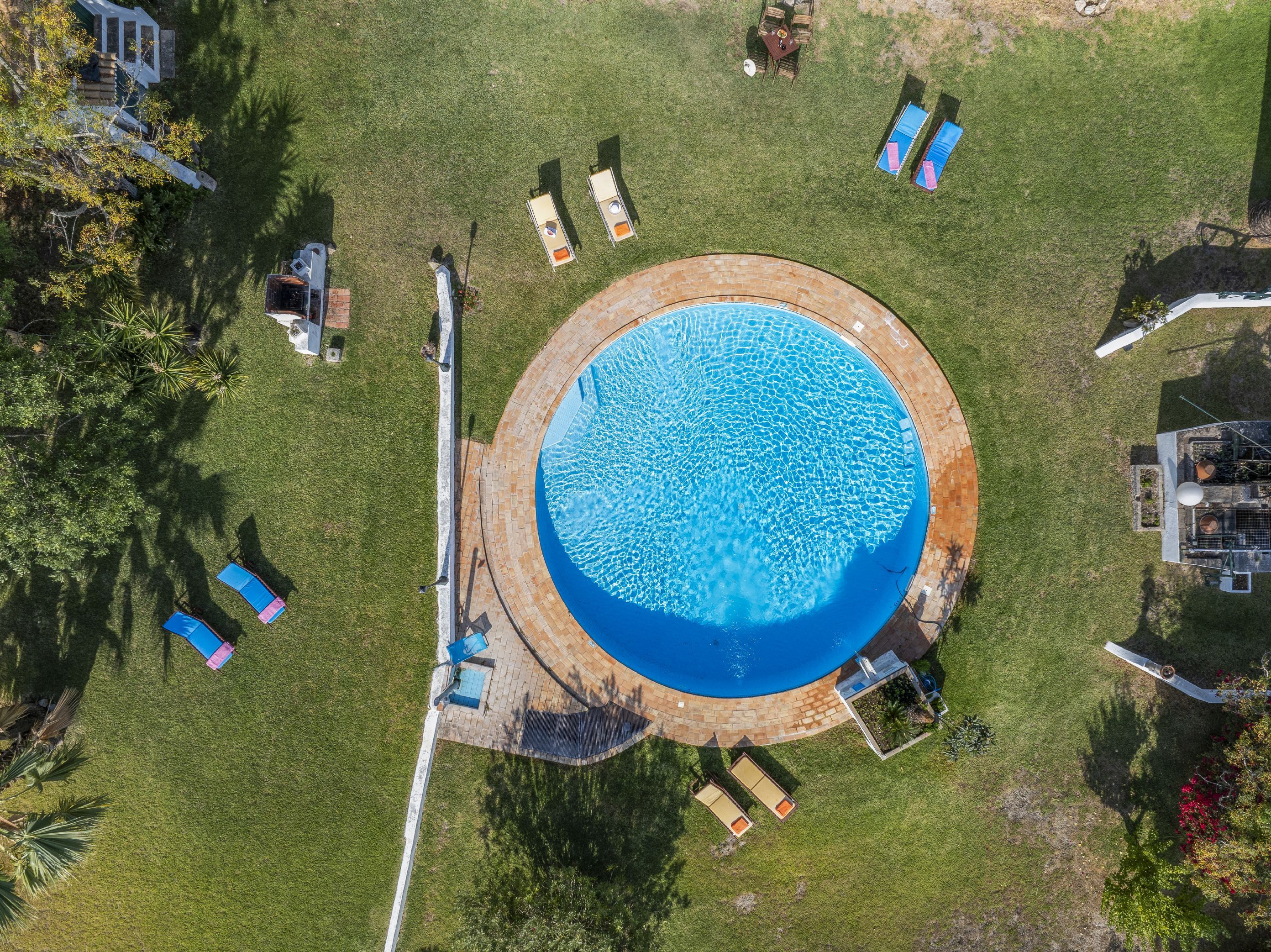 Vista aérea de una piscina circular con sillones de descanso y una zona de patio.