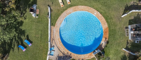 En vy från ovan av en rund swimmingpool med solstolar och en uteplats runt omkring.