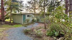 A small, single-story building with a green door, surrounded by trees and a gravel path. - NEW LISTING-Mutiny Bay Ebb Tide Cabin AMAZING SUNSETS, EAGLES GALORE SANDY BEACH (Freeland)