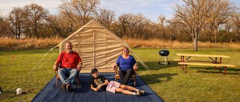 Une scène de camping avec une tente, une table de pique-nique et un champ d’herbe.