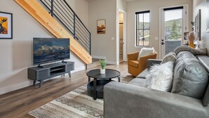 A modern living room with a staircase, a flat-screen TV, a sofa, and a coffee table. - Downtown WP Loft 57 I Rooftop Hot Tub & Lounge I Great Views I Bunk Room I Discounted Attractions (Winter Park)
