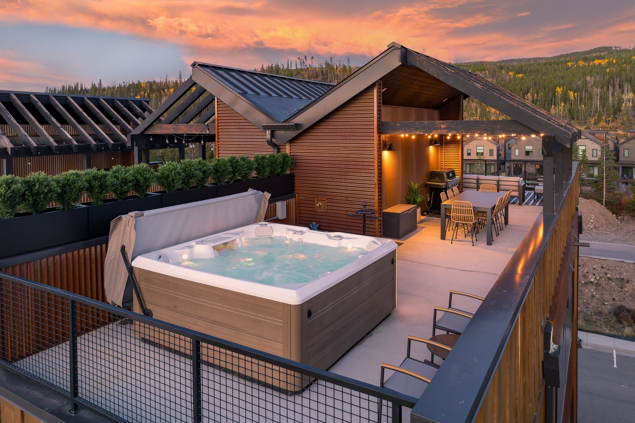 Ein moderner Außenbereich mit Whirlpool, einer Holzterrasse, Sitzgelegenheiten und Blick auf eine bewaldete Landschaft.