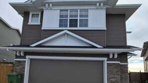 A two-story house with a garage, stone accents, and a sloped roof. - Quaint 2-bedroom house in Chestermere perfect for relaxing stays (Chestermere)