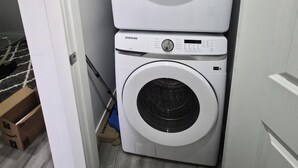 A stacked washer and dryer unit in a laundry room with a door leading to another room. - Quaint 2-bedroom house in Chestermere perfect for relaxing stays (Chestermere)