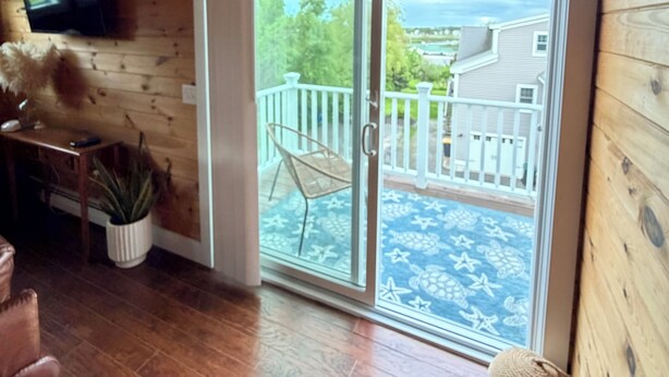 Interior em madeira com porta de vidro deslizante para uma varanda, televisão na parede e um vaso com planta.