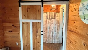 Interior em madeira com porta deslizante que dá para um quarto com cama e cortinas.