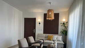 En stue med sofa, to lænestole, sofabord, hængende lampe, en dør og en plante.