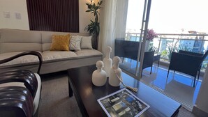 En moderne stue med sofa, sofabord med dekorative genstande, og udsigt til en balkon med udendørs møbler.