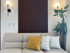 Een bank met drie kussens, een wandlamp, een houten paneel en een plant in een pot.