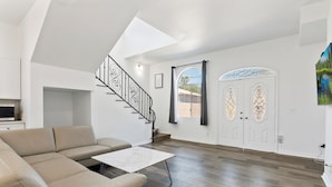 A modern living room with a sectional sofa, a glass coffee table, and a staircase with a black railing.
