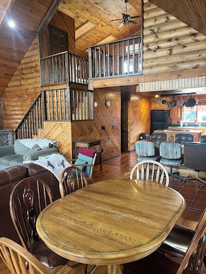 L’intérieur d’un chalet en bois comprend une table à manger, des chaises, un canapé, un coin cuisine et un escalier.