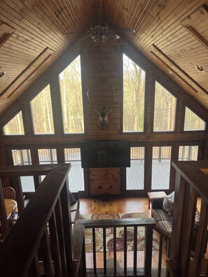 A wooden interior with a fireplace, large windows, and a deer head mounted on the wall.