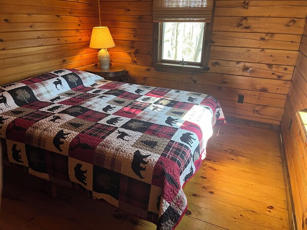A wooden cabin room with a bed, a lamp, and a window.