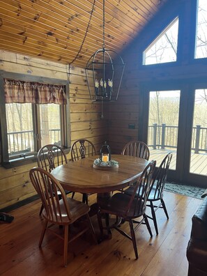 A wooden interior with a round dining table surrounded by chairs, a hanging light fixture, and large windows with a view of trees. - The Hawn Hideaway-3 mi to Seven Points Marina, sleeps 12 (Hesston)
