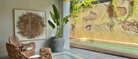 A room with wicker chairs, a large potted plant, and a wall with a water feature and greenery.