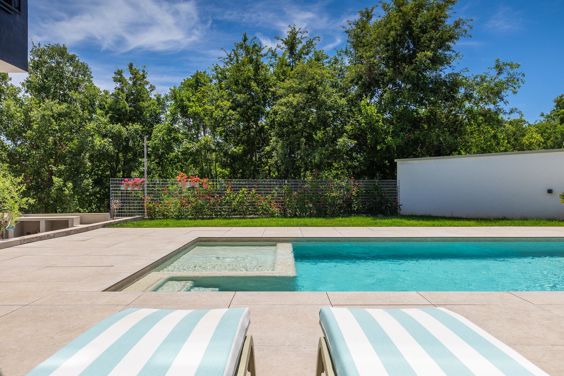 A swimming pool with two lounge chairs, surrounded by a fence and greenery.