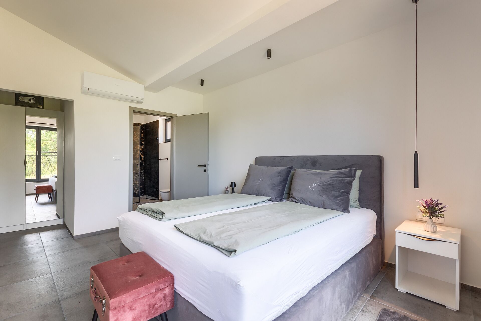 A modern bedroom with a large bed, a small bedside table, and a view of the outside.
