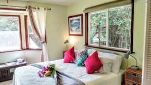 Une chambre à coucher avec un lit, des oreillers, une table de chevet, une lampe et une fenêtre donnant sur des arbres.