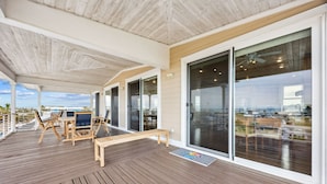 Une terrasse extérieure couverte avec un plancher en bois, une table et des chaises, ainsi que de grandes portes-fenêtres coulissantes.