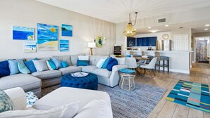 A modern living room with a sofa, ottoman, and artwork on the wall. - Coastal Condo Oasis | Walk to Beach (Fernandina Beach)