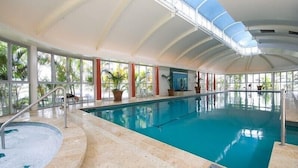 Une piscine intérieure avec des parois en verre transparent, des plantes en pot et un sol carrelé.