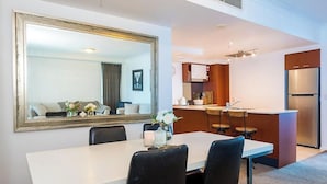 Une chambre d’hôtel moderne dotée d’un coin repas, d’un grand miroir, d’une cuisine avec réfrigérateur et d’un bar.
