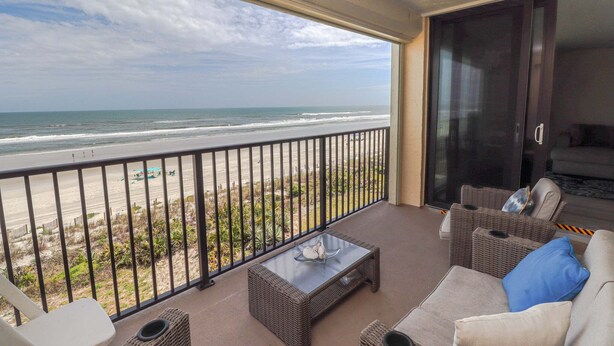 A balcony with a view of the beach, wicker furniture, and a glass coffee table. - Sand Dollar 1-407 Amazing Oceanfront Views from Private Balcony! (St. Augustine)