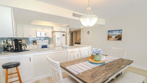 A modern kitchen with white cabinets, a wooden dining table, and a chandelier. - Sand Dollar 1-407 Amazing Oceanfront Views from Private Balcony! (St. Augustine)