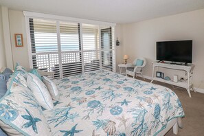 A bedroom with a bed, a TV, a chair, and a window with blinds. - Sand Dollar 1-407 Amazing Oceanfront Views from Private Balcony! (St. Augustine)