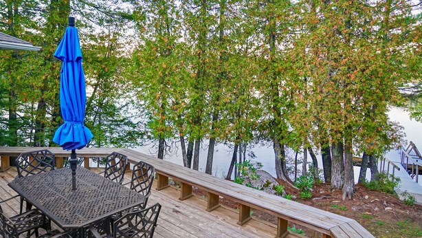 A wooden deck with a table and chairs, overlooking a body of water with trees.