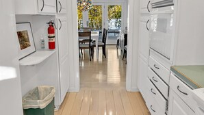 A narrow hallway with white cabinetry, a fire extinguisher, a trash bin, and a dining area with chairs and a table.