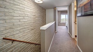 A hallway with a brick wall, a ceiling light, a wooden handrail, and a door leading to a room with a window. - Charming Coral Cay #207: 2BR condo with pool view in Port Aransas. (Port Aransas)