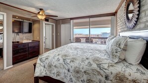 A bedroom with a large bed, a ceiling fan, a TV, a dresser, and a balcony with a view. - Charming Coral Cay #207: 2BR condo with pool view in Port Aransas. (Port Aransas)